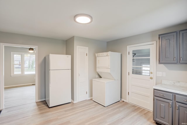 laundry area with light hardwood / wood-style floors, stacked washer / dryer, and ceiling fan