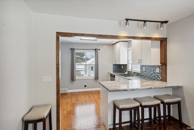 kitchen featuring sink, light hardwood / wood-style flooring, white cabinetry, kitchen peninsula, and a breakfast bar area