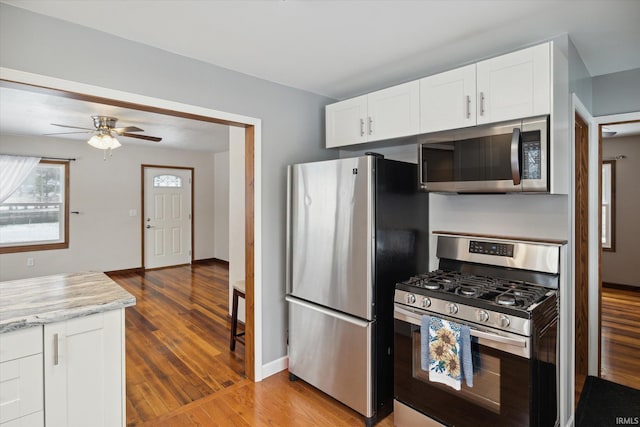 kitchen with light stone countertops, white cabinetry, stainless steel appliances, and wood-type flooring