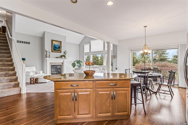 kitchen with a center island, hanging light fixtures, vaulted ceiling, dark hardwood / wood-style floors, and light stone countertops