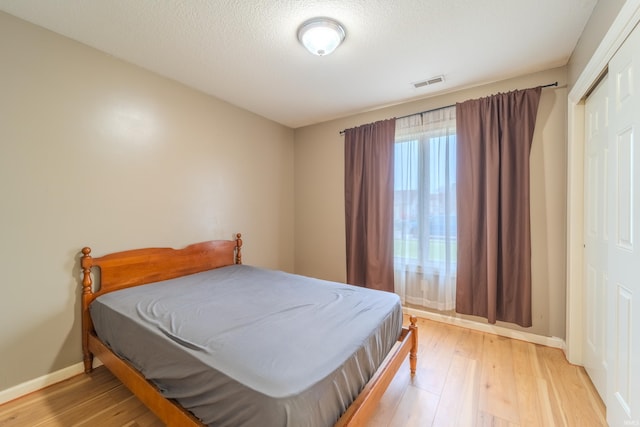 bedroom featuring a closet, light hardwood / wood-style flooring, and a textured ceiling