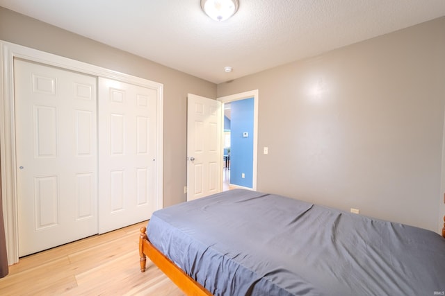 bedroom with a textured ceiling, light hardwood / wood-style flooring, and a closet