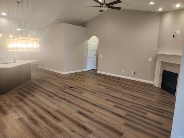 unfurnished living room with dark wood-type flooring, a tile fireplace, sink, vaulted ceiling, and ceiling fan