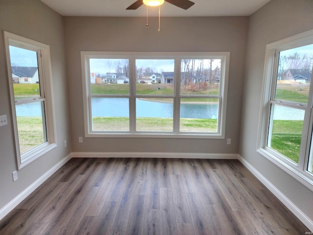 unfurnished room featuring dark hardwood / wood-style flooring, ceiling fan, plenty of natural light, and a water view