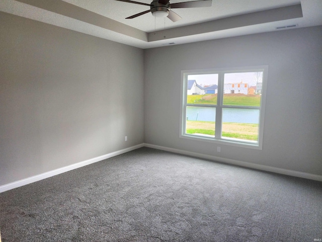 spare room with a raised ceiling, carpet flooring, ceiling fan, and a water view