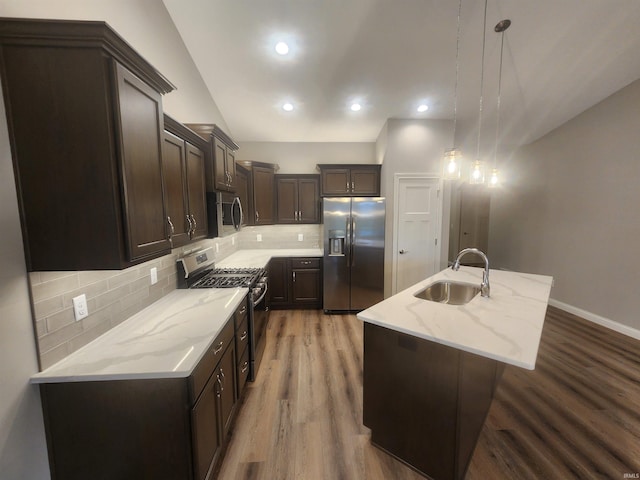 kitchen featuring sink, hanging light fixtures, stainless steel appliances, backsplash, and an island with sink