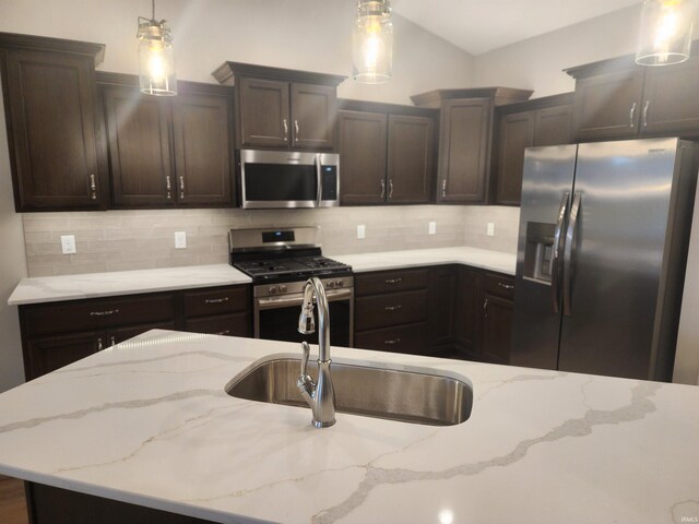 kitchen with light stone countertops, sink, hanging light fixtures, backsplash, and appliances with stainless steel finishes