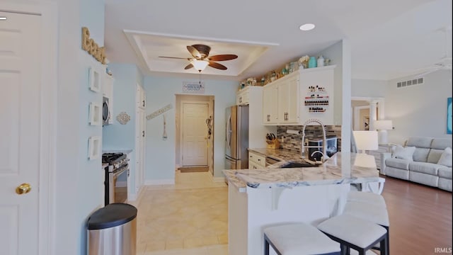 kitchen featuring kitchen peninsula, a kitchen breakfast bar, light stone countertops, stainless steel appliances, and white cabinetry