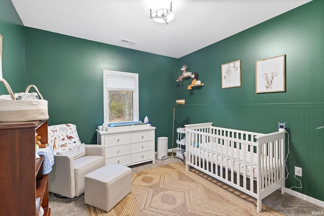 bedroom featuring a textured ceiling, a crib, and light carpet