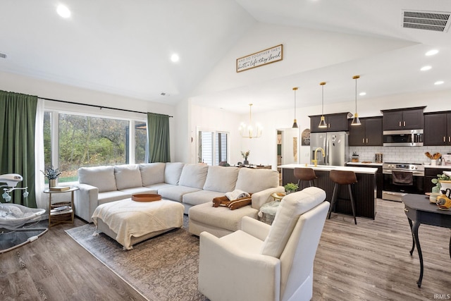 living room featuring a chandelier, high vaulted ceiling, and light hardwood / wood-style flooring