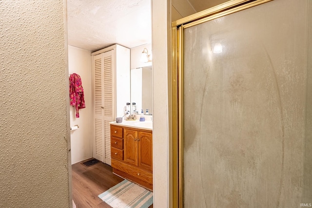 bathroom featuring hardwood / wood-style floors, vanity, a textured ceiling, and walk in shower