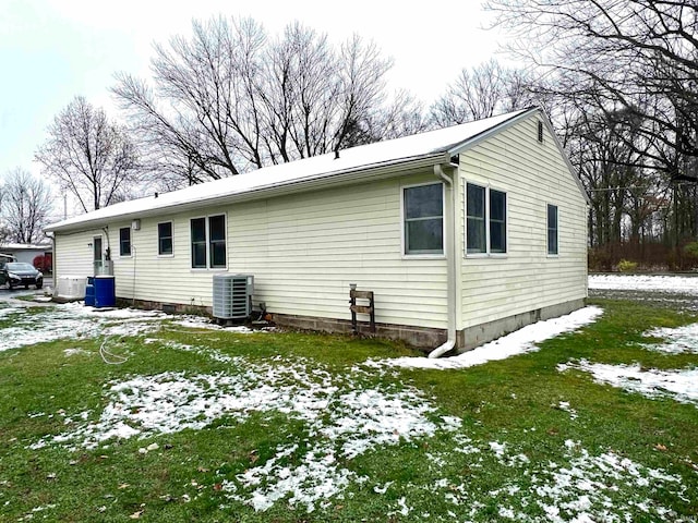 snow covered rear of property featuring central AC unit and a lawn