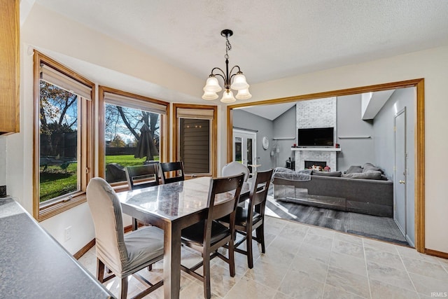 tiled dining area featuring a textured ceiling, vaulted ceiling, a notable chandelier, and a stone fireplace