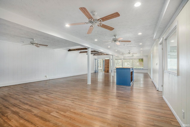 unfurnished living room featuring wooden walls, light hardwood / wood-style flooring, ceiling fan, and a textured ceiling