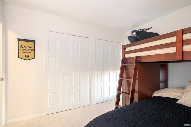 bedroom featuring light colored carpet and multiple closets