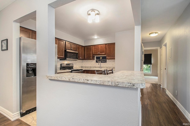 kitchen featuring sink, stainless steel appliances, dark hardwood / wood-style floors, kitchen peninsula, and decorative backsplash