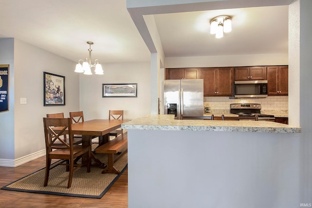 kitchen with appliances with stainless steel finishes, backsplash, a chandelier, hardwood / wood-style floors, and hanging light fixtures