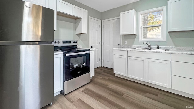 kitchen with sink, light stone countertops, light hardwood / wood-style floors, white cabinetry, and stainless steel appliances