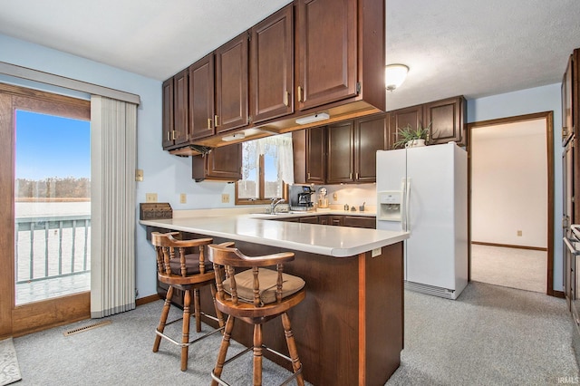 kitchen with a kitchen bar, white refrigerator with ice dispenser, kitchen peninsula, and a wealth of natural light