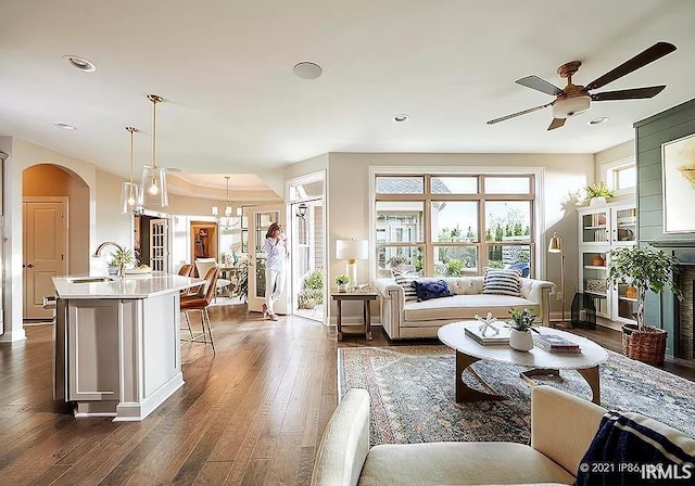 living room featuring ceiling fan with notable chandelier, dark wood-type flooring, and sink