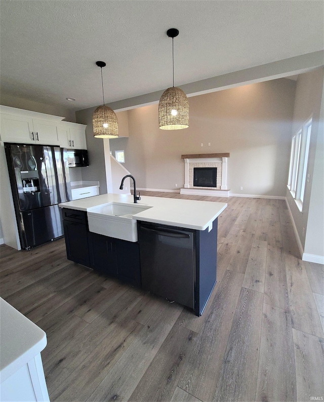 kitchen featuring sink, an island with sink, pendant lighting, light hardwood / wood-style floors, and black appliances