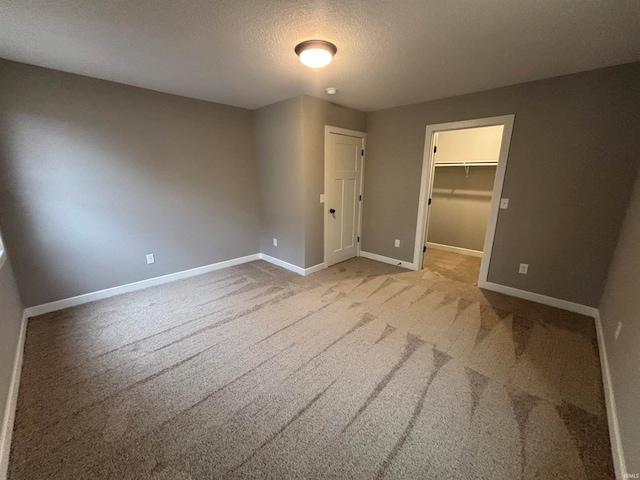 unfurnished bedroom featuring light carpet, a textured ceiling, a walk in closet, and a closet