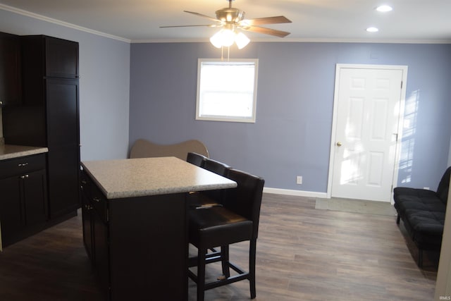 kitchen featuring ceiling fan, a center island, dark hardwood / wood-style floors, a kitchen bar, and ornamental molding