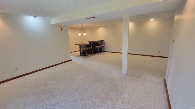 basement featuring light carpet, bar, and an inviting chandelier