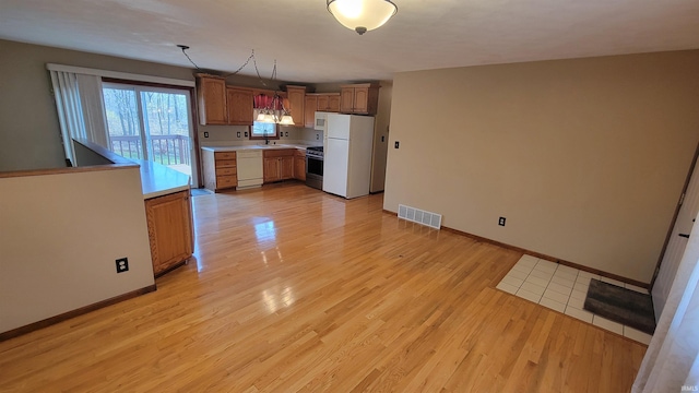 kitchen with light hardwood / wood-style flooring, pendant lighting, white appliances, and sink