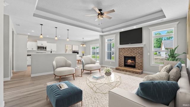 living room featuring a fireplace, ceiling fan with notable chandelier, light hardwood / wood-style floors, and a raised ceiling