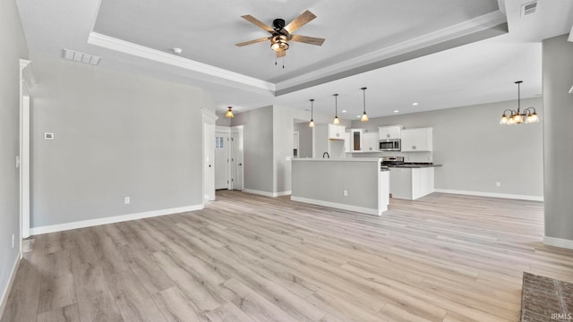 unfurnished living room with ceiling fan with notable chandelier, light hardwood / wood-style floors, crown molding, and a tray ceiling