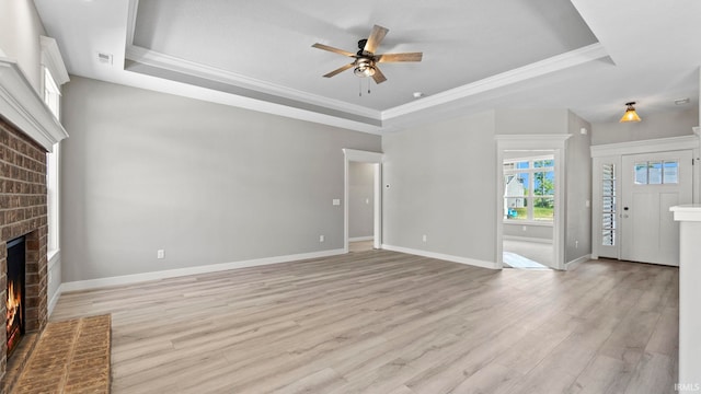 unfurnished living room featuring a fireplace, light wood-type flooring, a raised ceiling, and ceiling fan