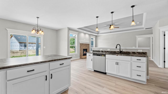 kitchen featuring white cabinetry, a raised ceiling, stainless steel dishwasher, light hardwood / wood-style floors, and ceiling fan with notable chandelier