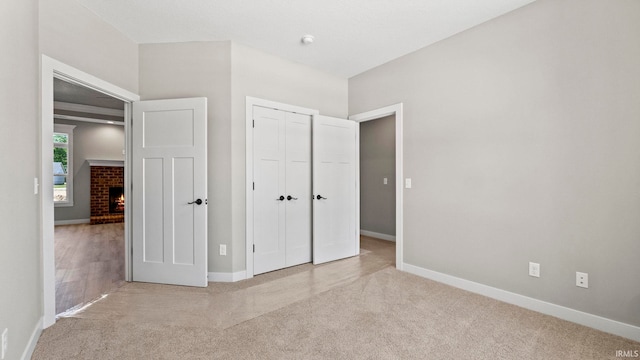 unfurnished bedroom with light carpet, a closet, and a fireplace