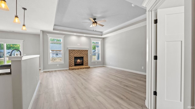 unfurnished living room with light hardwood / wood-style flooring, ceiling fan, a textured ceiling, a fireplace, and a tray ceiling