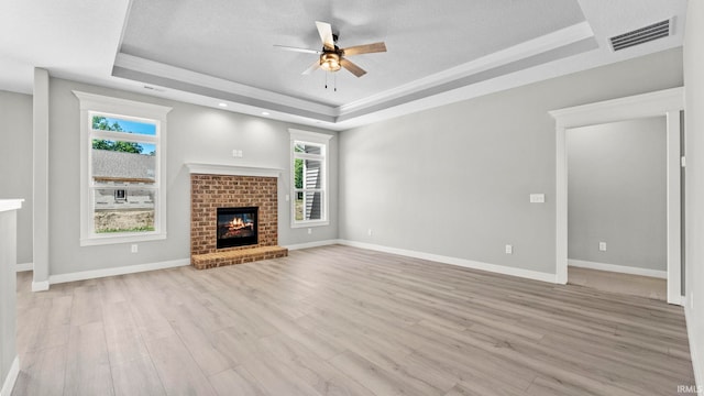 unfurnished living room featuring a tray ceiling, ceiling fan, light hardwood / wood-style flooring, and a brick fireplace