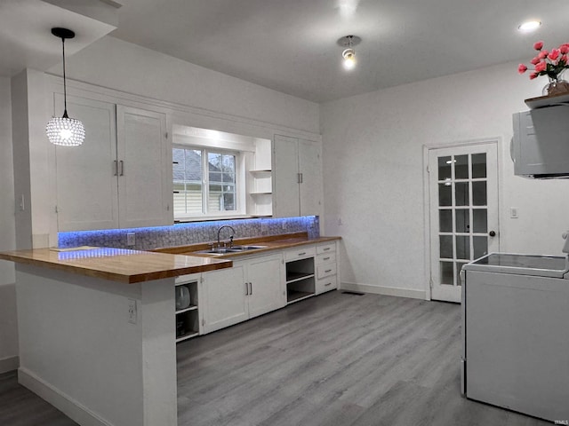 kitchen featuring butcher block counters, white cabinetry, washer / clothes dryer, kitchen peninsula, and decorative light fixtures