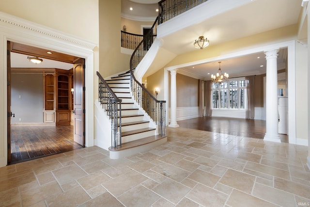 stairs with ornate columns, an inviting chandelier, wood-type flooring, and ornamental molding