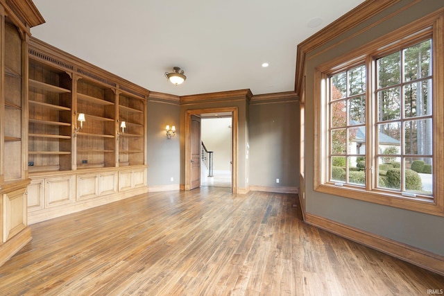 unfurnished living room featuring wood-type flooring, ornamental molding, and a healthy amount of sunlight