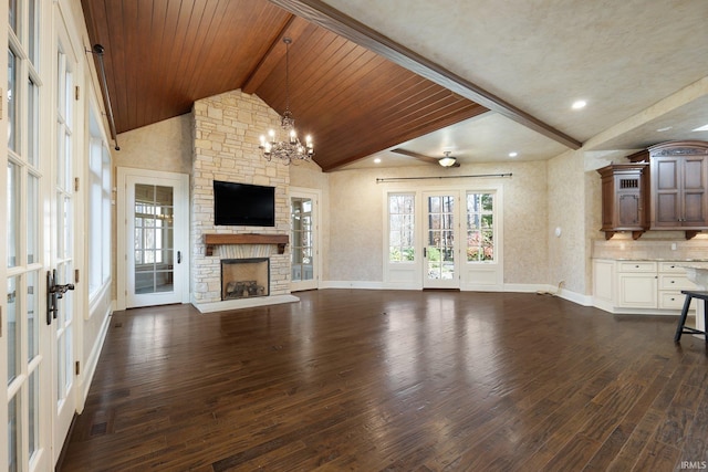 unfurnished living room with french doors, dark wood-type flooring, a stone fireplace, vaulted ceiling with beams, and ceiling fan with notable chandelier