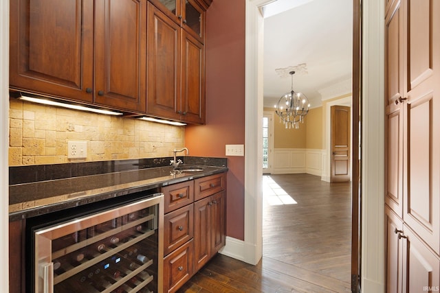 bar with decorative backsplash, beverage cooler, crown molding, dark wood-type flooring, and dark stone countertops