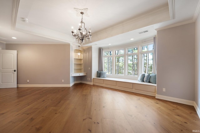 unfurnished living room with a raised ceiling, wood-type flooring, ornamental molding, and a chandelier