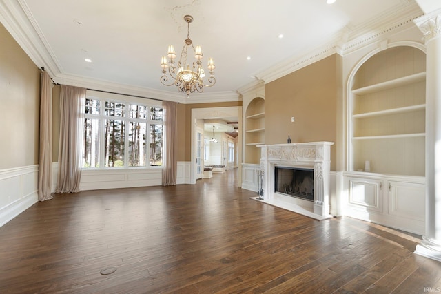 unfurnished living room featuring built in shelves, an inviting chandelier, ornamental molding, and dark wood-type flooring