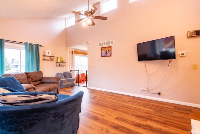 living room with a towering ceiling, ceiling fan, a wealth of natural light, and hardwood / wood-style floors