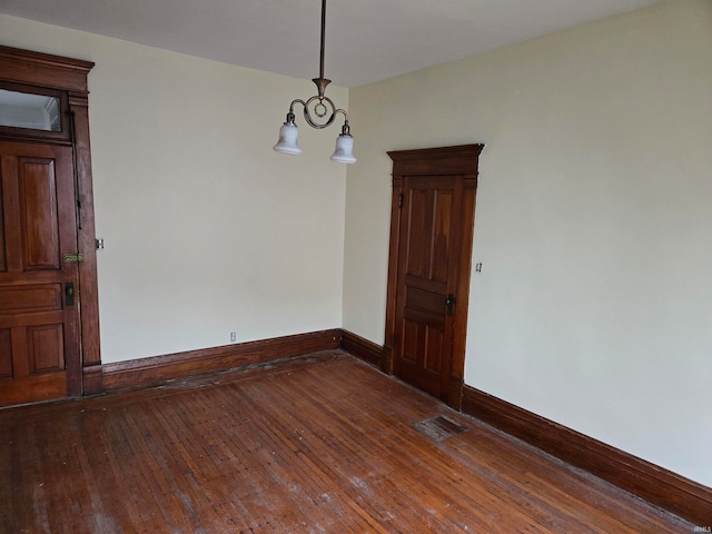 spare room featuring a chandelier and dark wood-type flooring