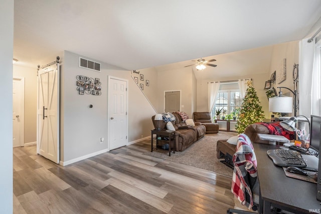 living room with ceiling fan, a barn door, and wood-type flooring