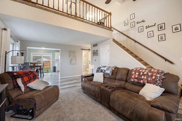 living room featuring ceiling fan, a barn door, light wood-type flooring, and a high ceiling