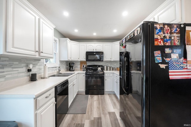 kitchen with backsplash, black appliances, white cabinets, sink, and light hardwood / wood-style floors