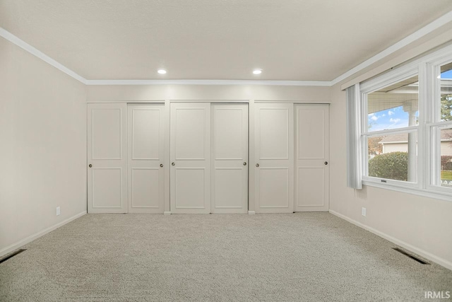 unfurnished bedroom featuring crown molding, light colored carpet, and two closets