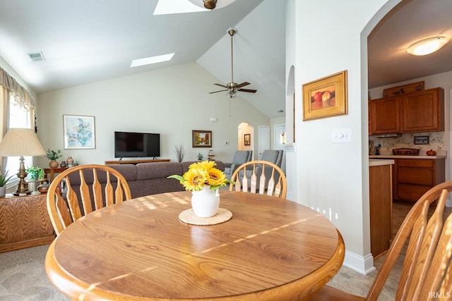 dining space with ceiling fan, high vaulted ceiling, and a skylight